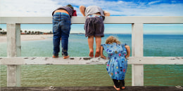 Rear view of siblings looking at sea while standing on railing against sky