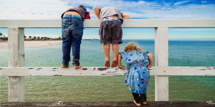 Rear view of siblings looking at sea while standing on railing against sky
